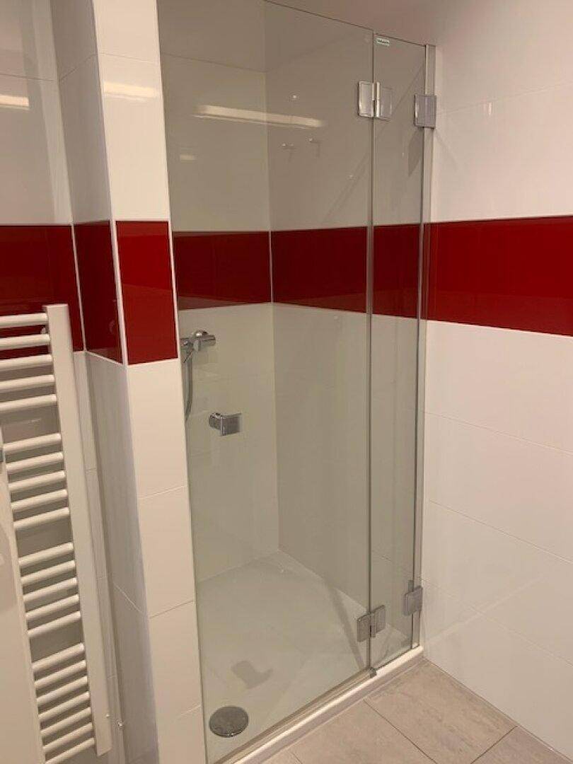 Modernes Badezimmer mit begehbarer Dusche, Glasabtrennung und weiß-roten Fliesen.
