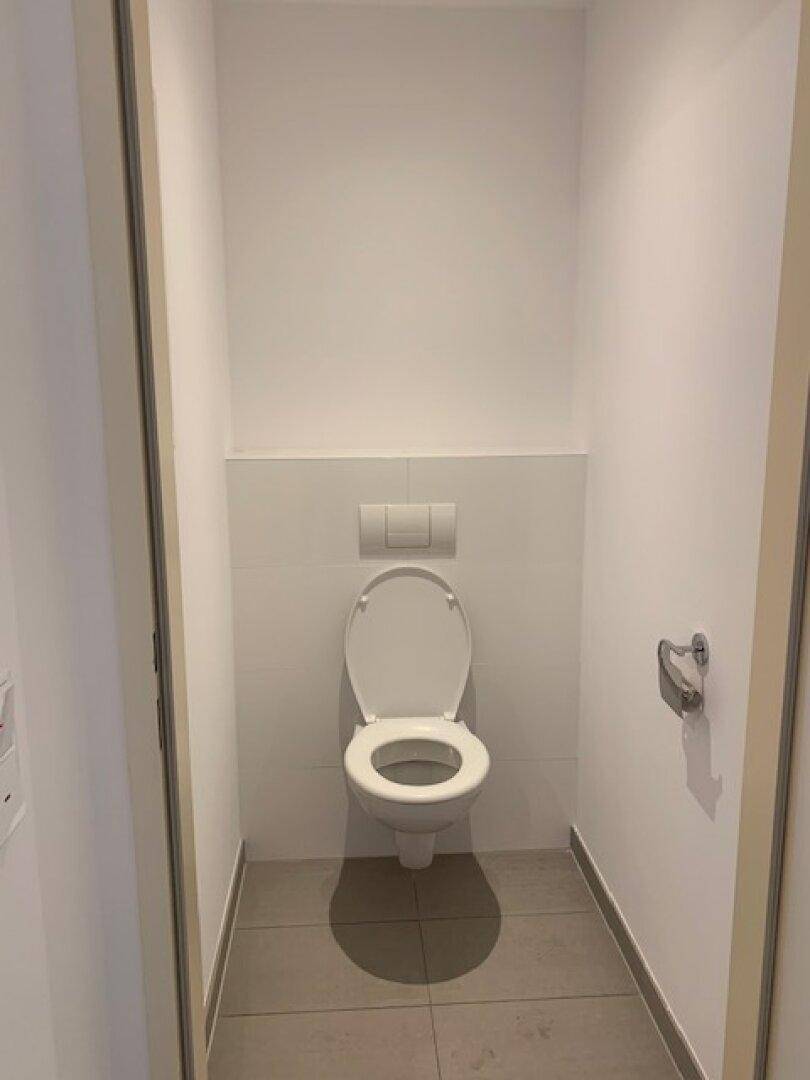 Separates WC mit wandmontierter Toilette und hellen Fliesen, funktional und sauber.