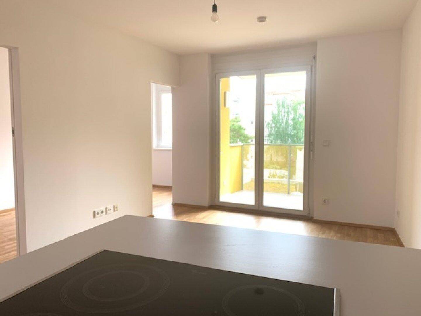Heller Wohnbereich mit Holzboden und Zugang zu einem Balkon, der viel Tageslicht hereinlässt.