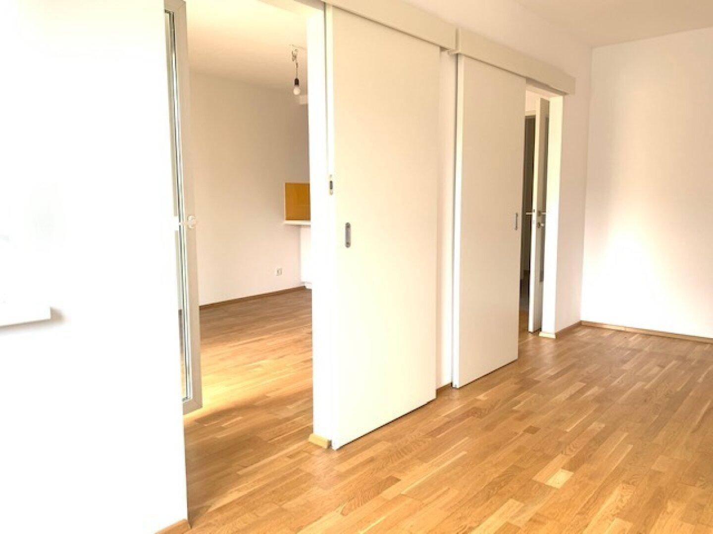 Heller Wohnbereich mit Schiebetüren und Holzboden, der zu weiteren Räumen führt.