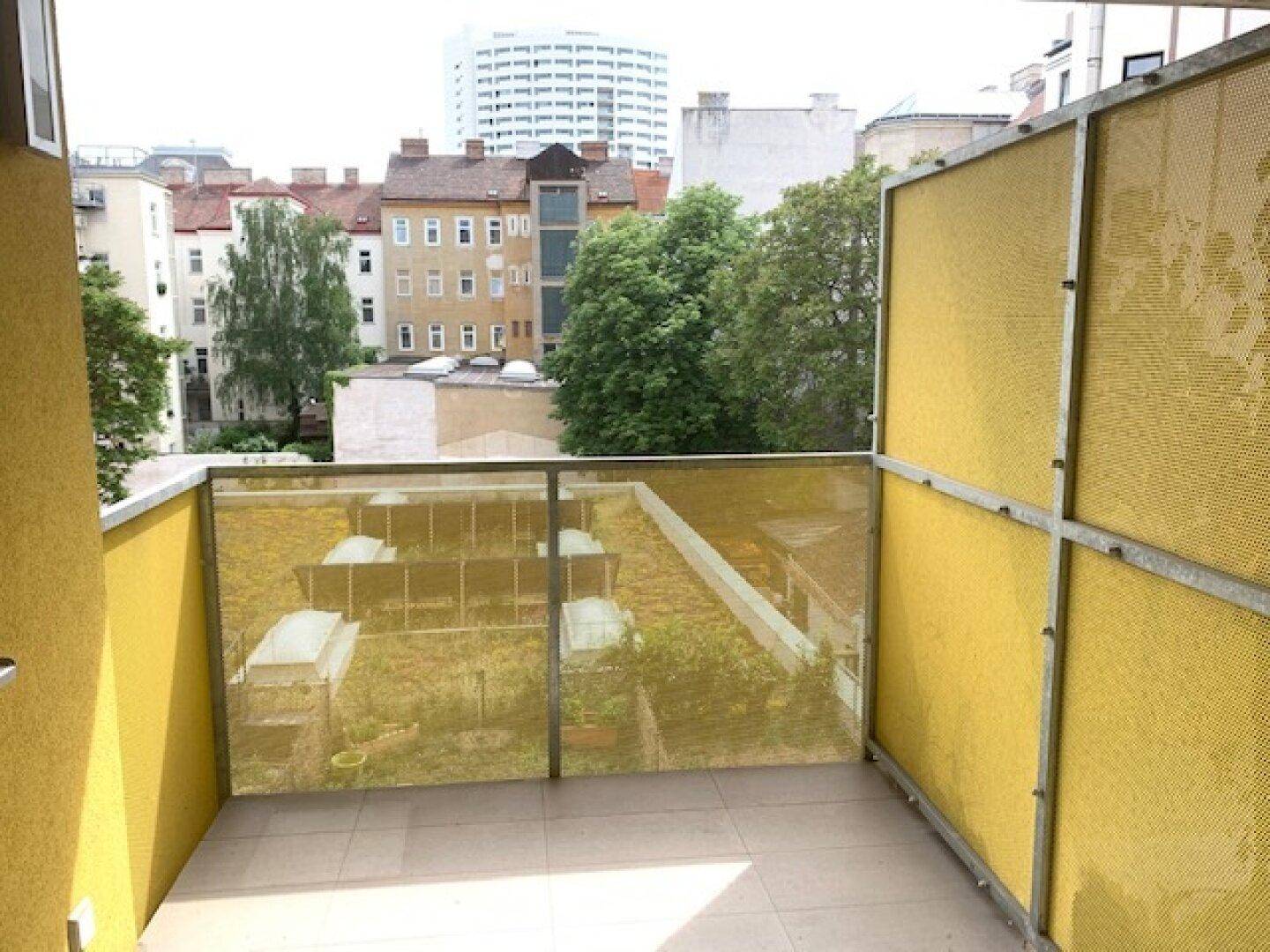 Heller Balkon mit Fliesenboden und gelben Sichtschutzelementen, bietet einen Blick auf die Stadt.