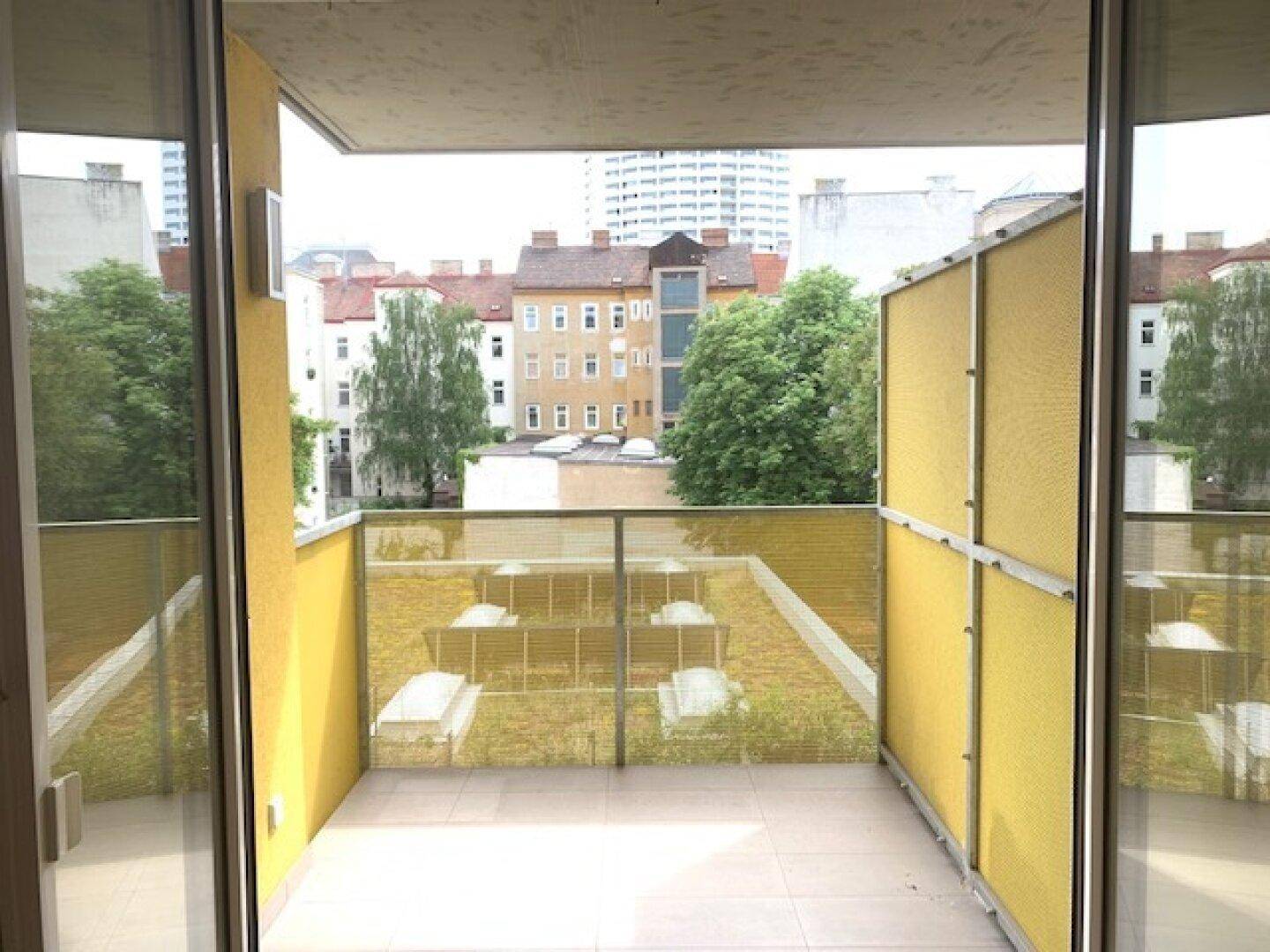 Balkon mit gelben Sichtschutzelementen und Blick auf die umliegenden Gebäude und Grünflächen.