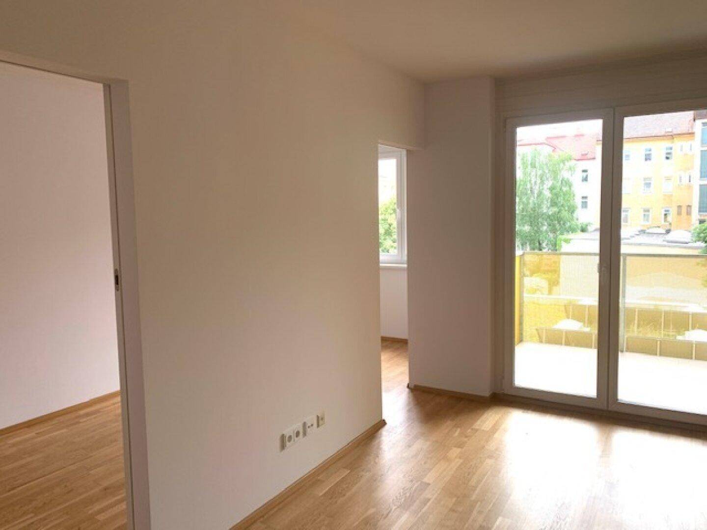 Geräumiger Wohnbereich mit Holzboden und großen Fenstern, die viel Tageslicht bieten.