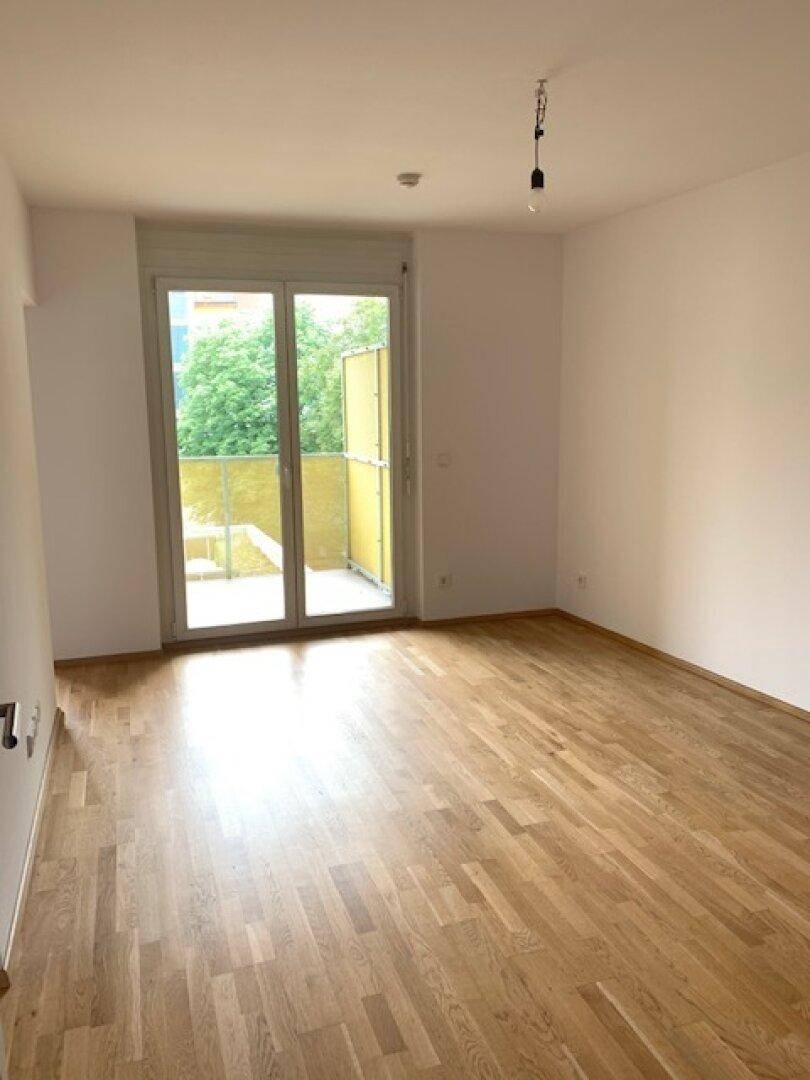 Heller Wohnbereich mit Holzboden und Balkonzugang, der eine angenehme Wohnatmosphäre schafft.