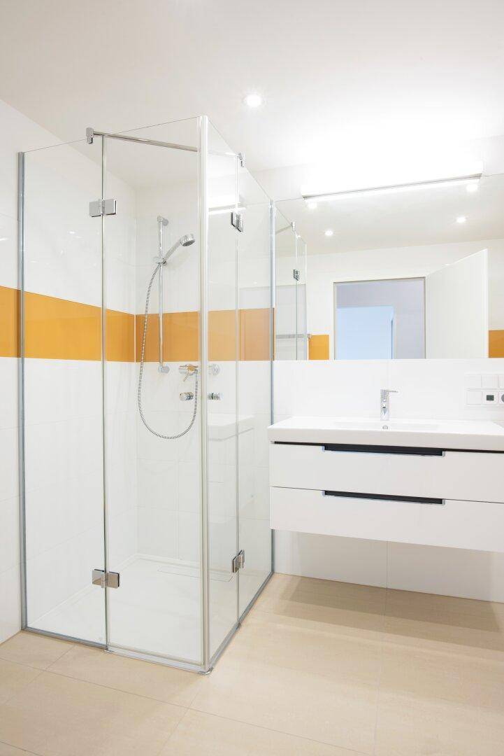 Modernes Badezimmer mit begehbarer Dusche, Waschtisch und orangefarbenem Akzentstreifen.