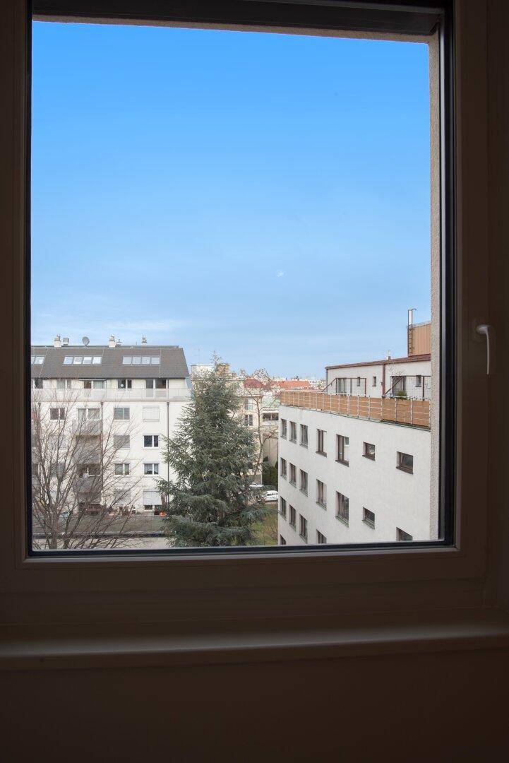 Blick aus dem Fenster auf die umliegenden Gebäude und den blauen Himmel.