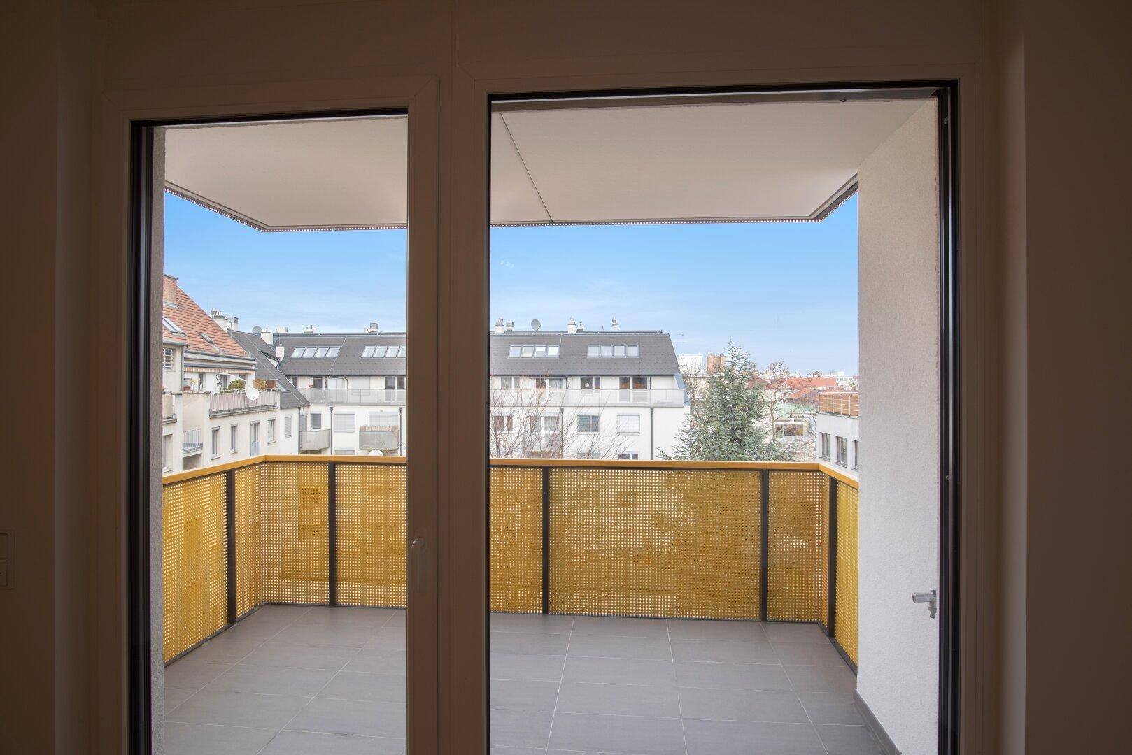 Blick vom Wohnbereich auf den Balkon mit moderner gelochter Brüstung und Stadtansicht.