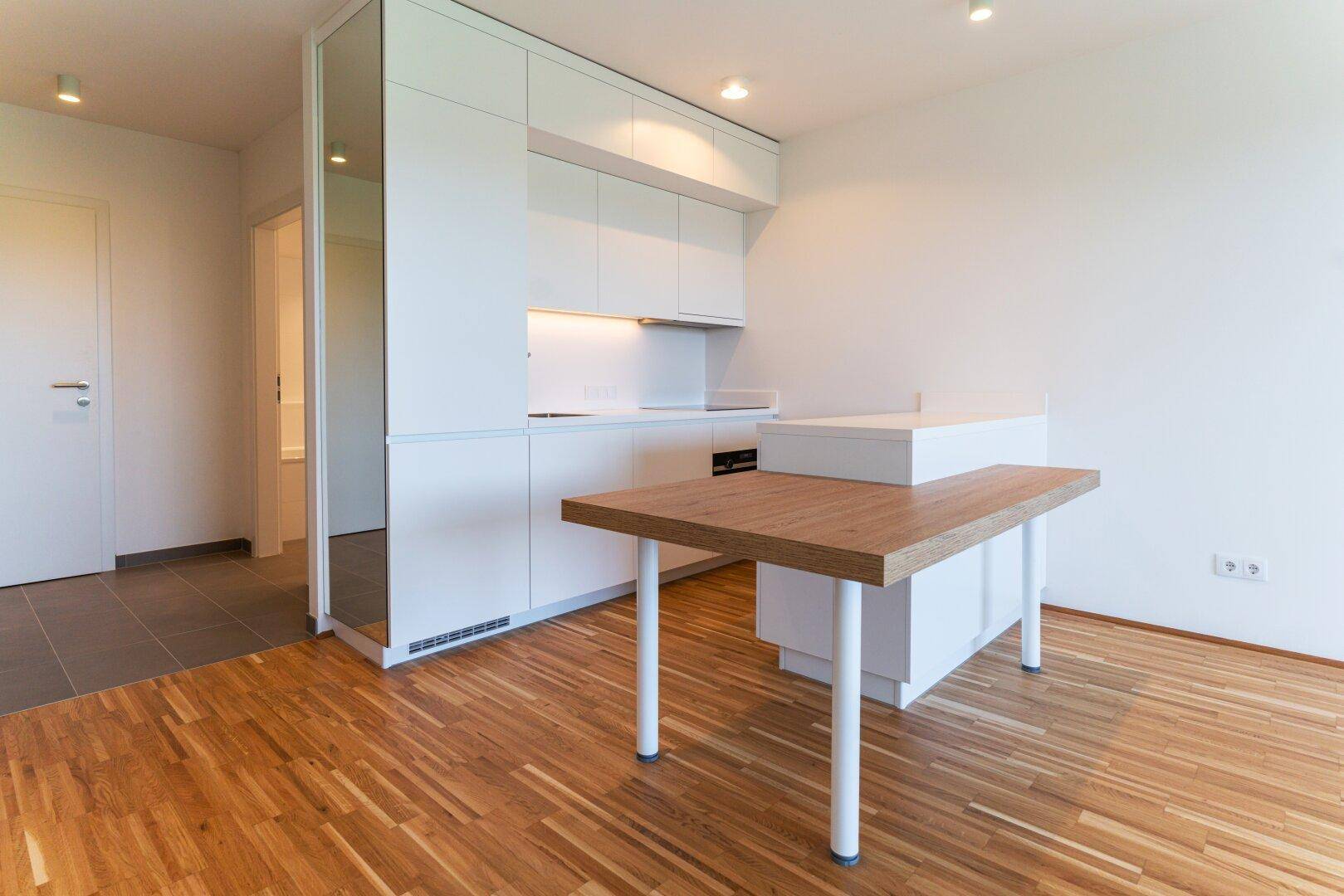 Moderne Küchenzeile mit Holztisch und Parkettboden in einem hellen, offenen Wohnbereich.