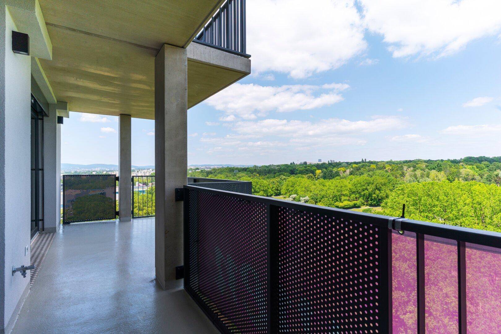 Geräumiger Balkon mit weitem Blick über grüne Baumwipfel und die Stadt am Horizont.