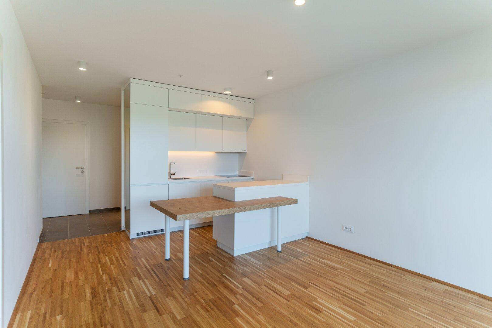 Helle, offene Küchenzeile mit integriertem Esstisch und modernem Parkettboden in der Wohnung.