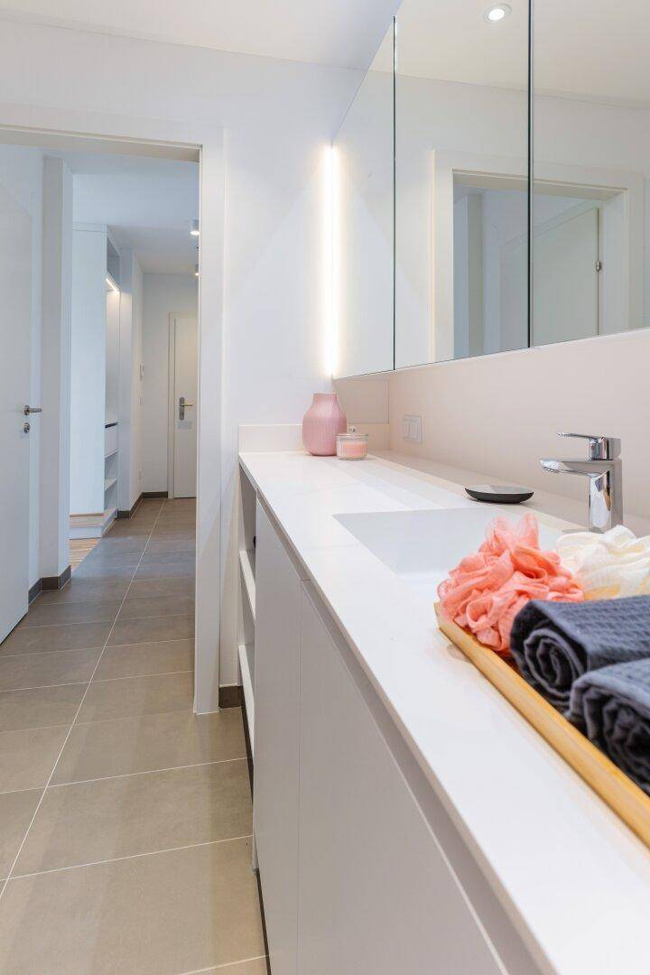 Modernes Badezimmer mit elegantem Waschtisch, integriertem Waschbecken und Spiegelschrank, verbunden mit einem hellen Flur.