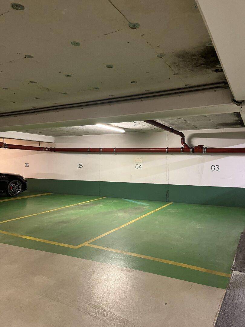 Tiefgarage mit markierten Parkplätzen und roten Rohren entlang der Wand.
