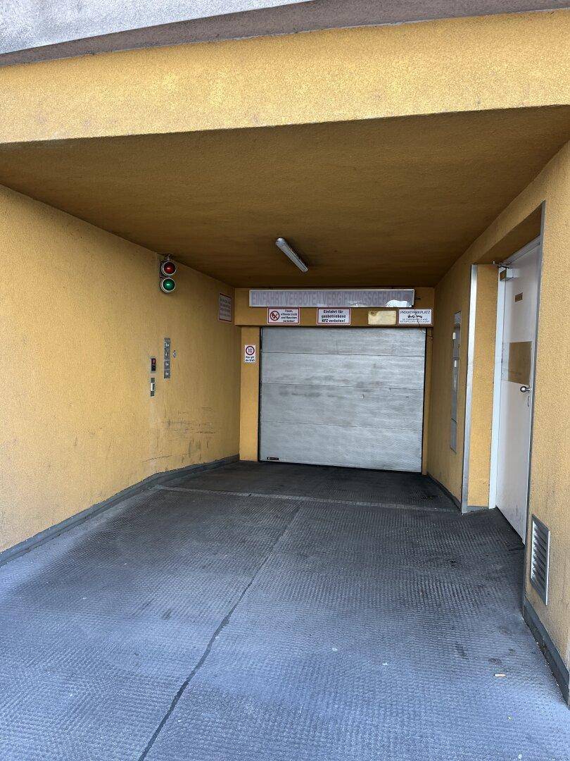 Einfahrt zu einer Tiefgarage mit geschlossenem Tor und gelben Wänden.