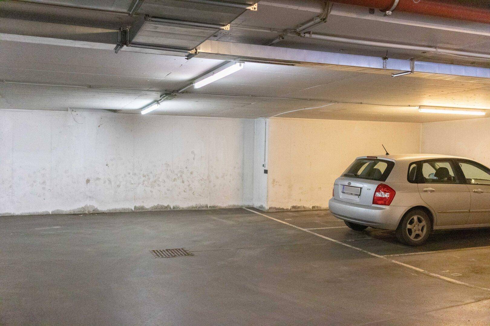 Geräumige Tiefgarage mit einem geparkten Auto und mehreren leeren Stellplätzen unter hellen Leuchtstoffröhren.