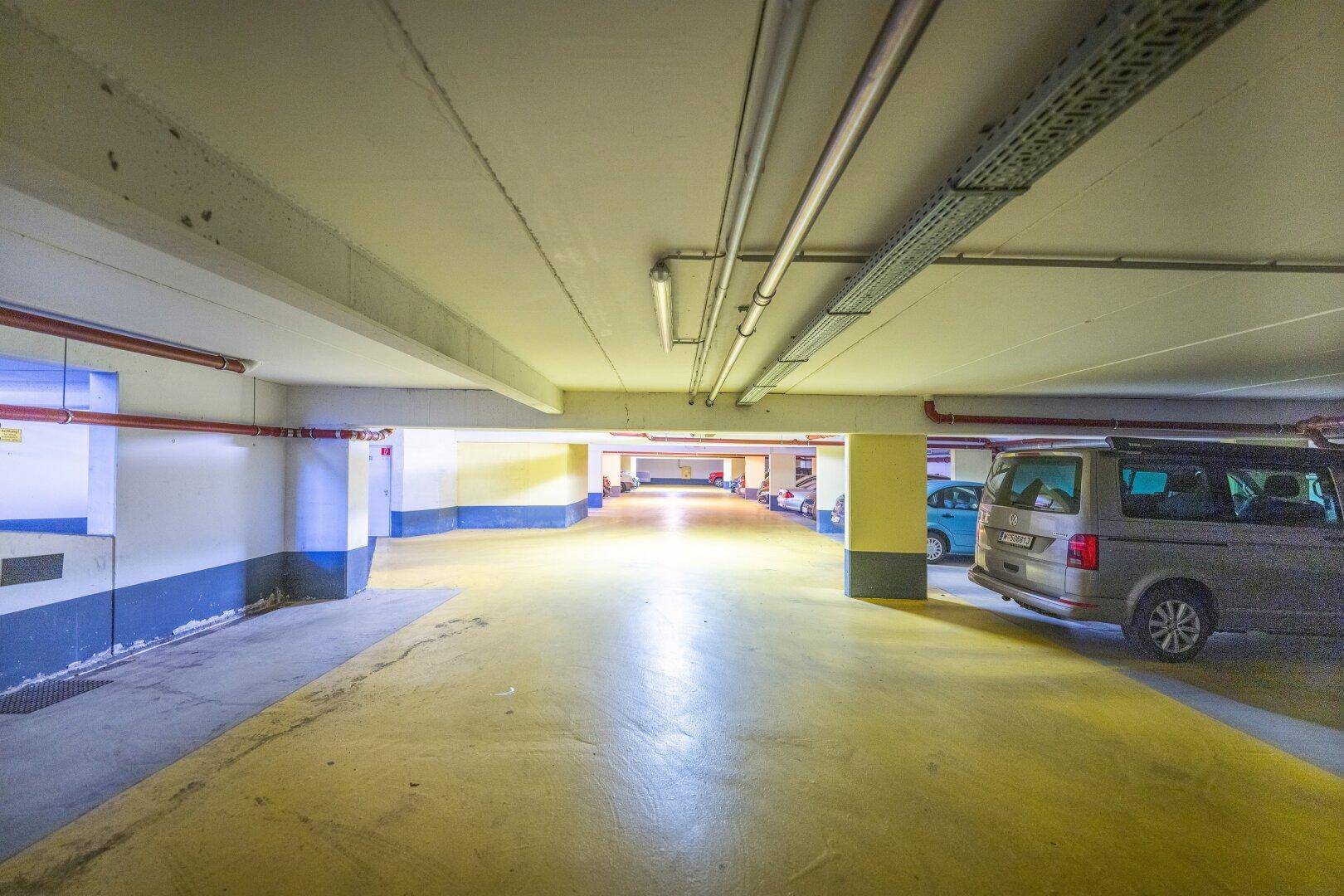 Lange Tiefgarage mit gelb markiertem Boden, zahlreichen Stellplätzen und Deckeninstallationen.