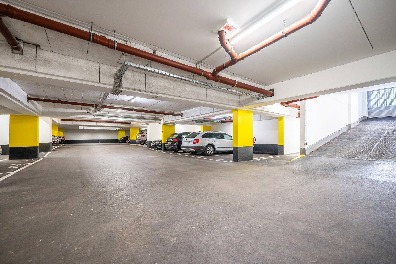 Geräumige Tiefgarage mit vielen Stellplätzen, gelben Stützen und guter Beleuchtung.