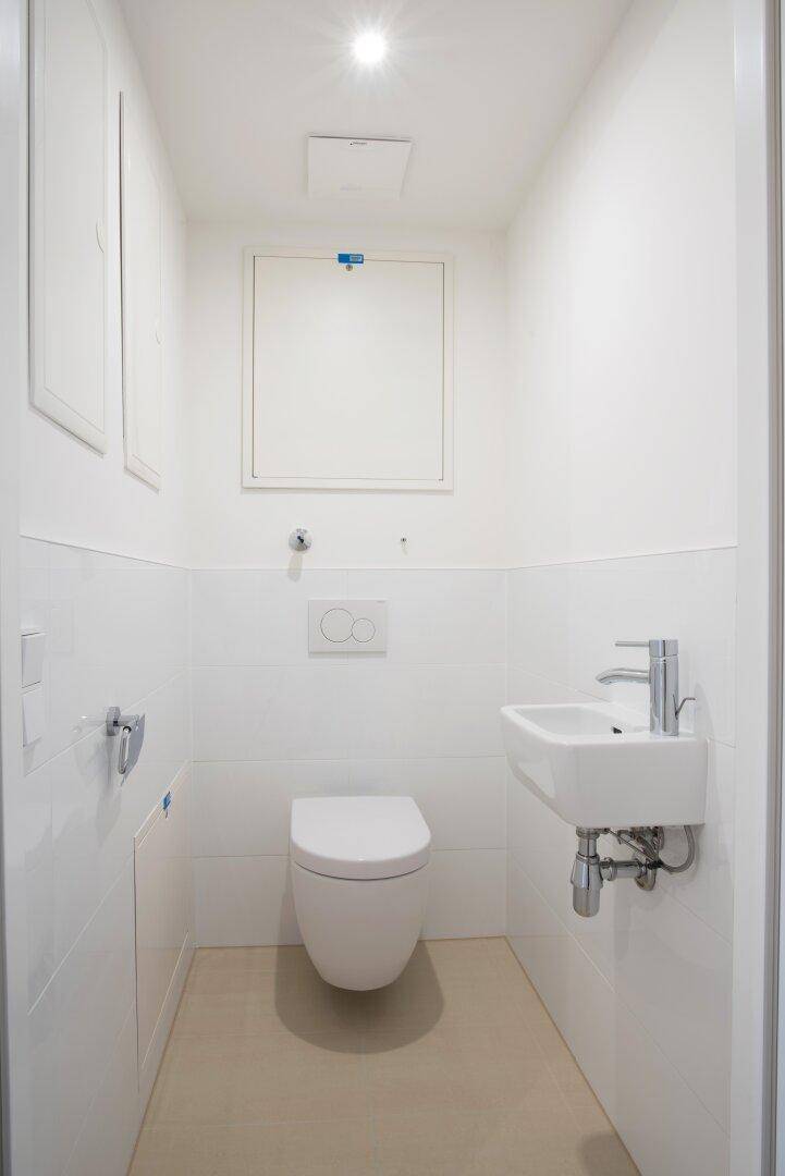 Kleines Gäste-WC mit wandhängendem WC, Handwaschbecken und hellen Fliesen.