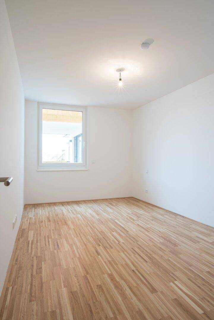Helles Zimmer mit Parkettboden und großem Fenster, ideal als Schlaf- oder Arbeitszimmer.