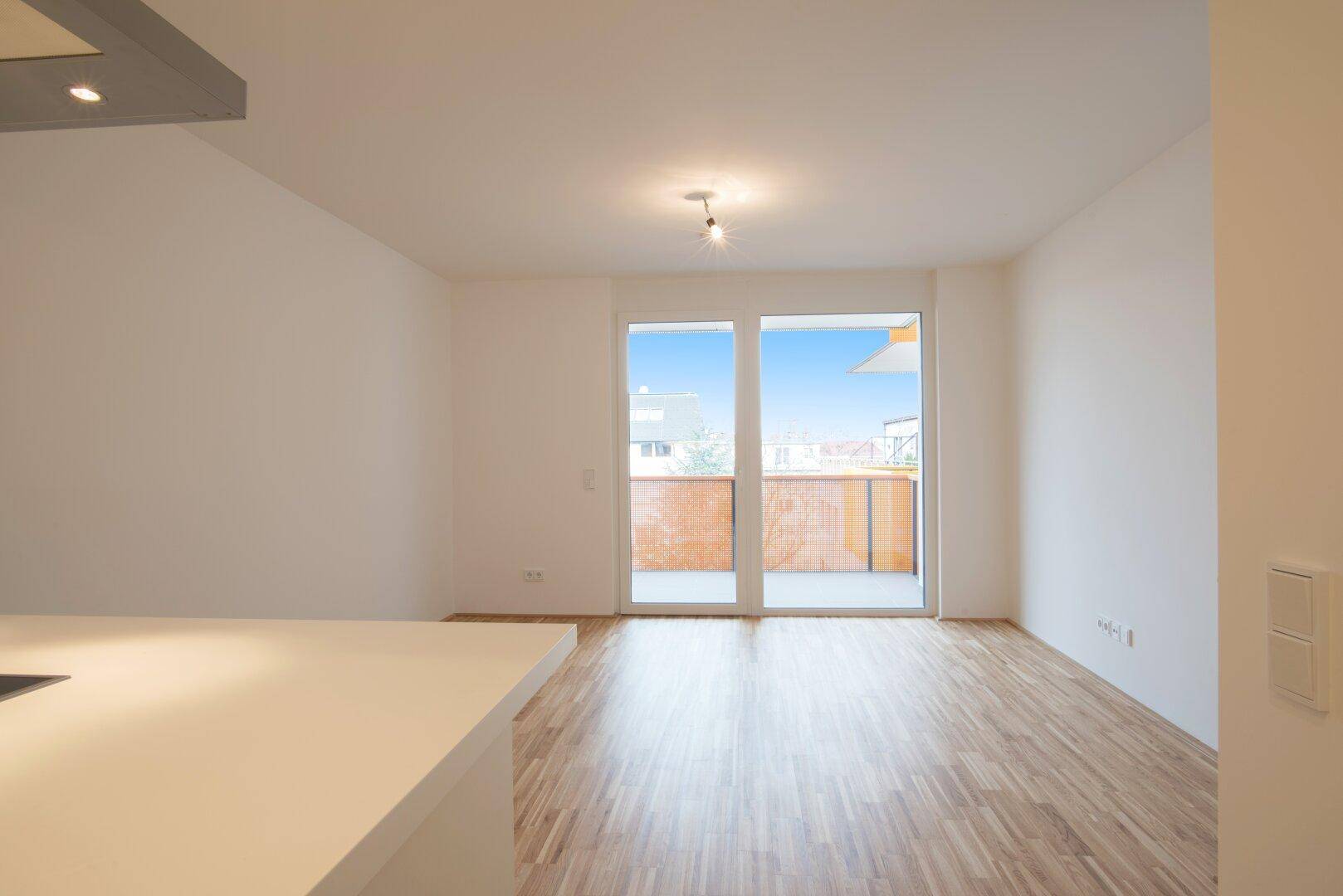 Lichtdurchfluteter Wohnbereich mit Zugang zum Balkon und hellem Parkettboden.