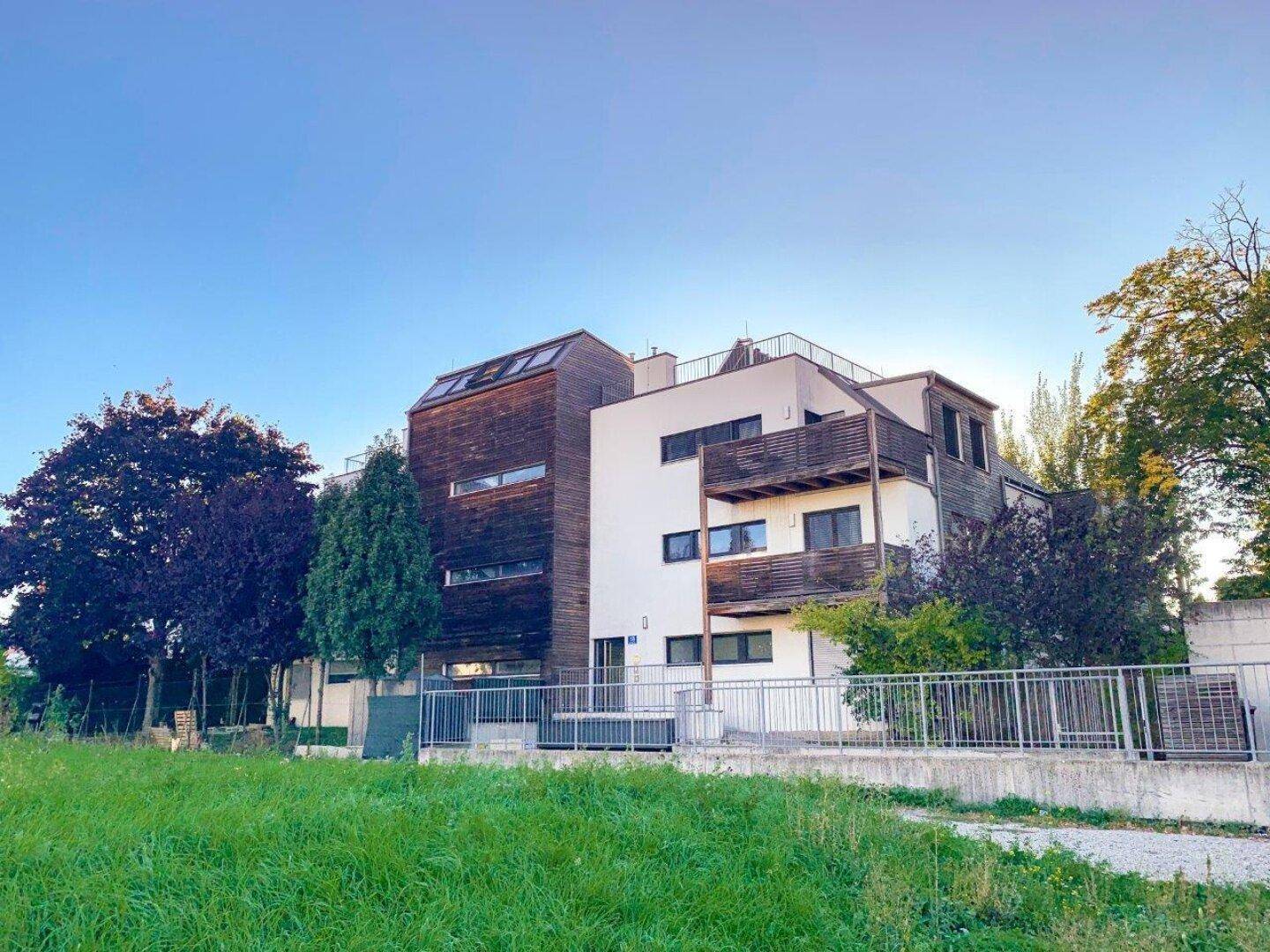 Modernes Wohngebäude mit Holzverkleidung und Balkonen, eingebettet in grüne Umgebung.