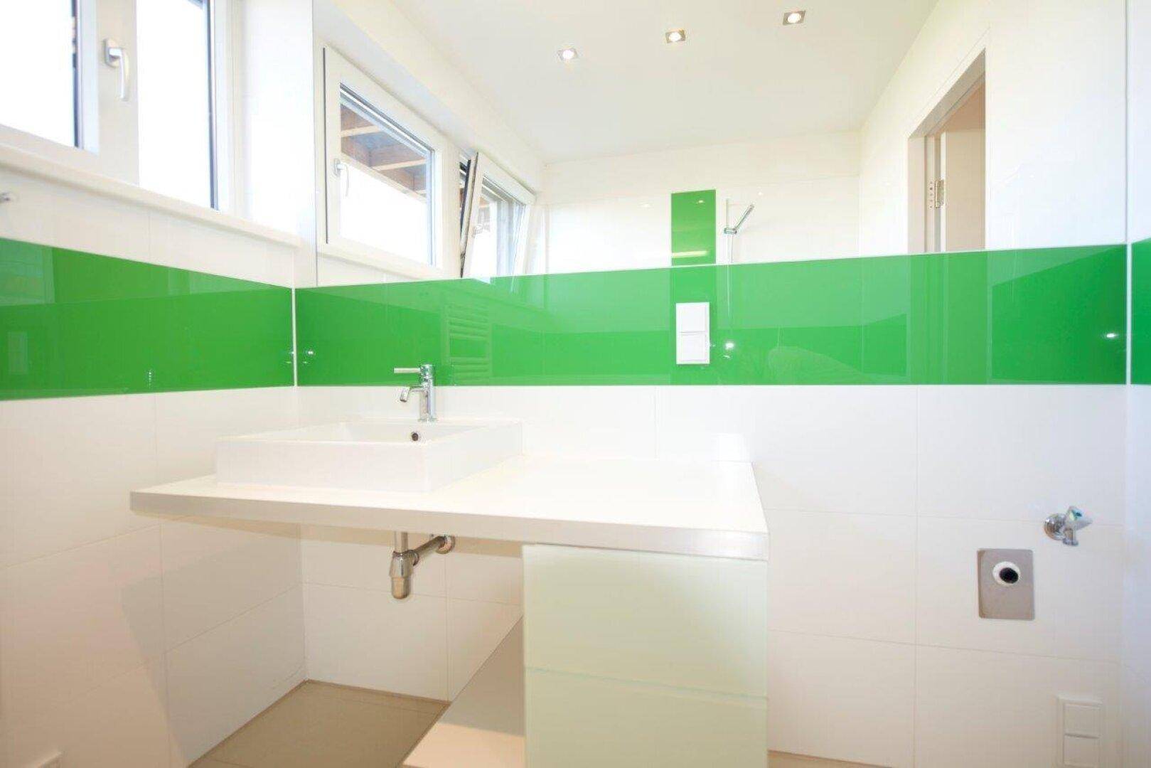 Modernes Badezimmer mit Einzelwaschbecken, großem Spiegel und grünen Wandelementen.