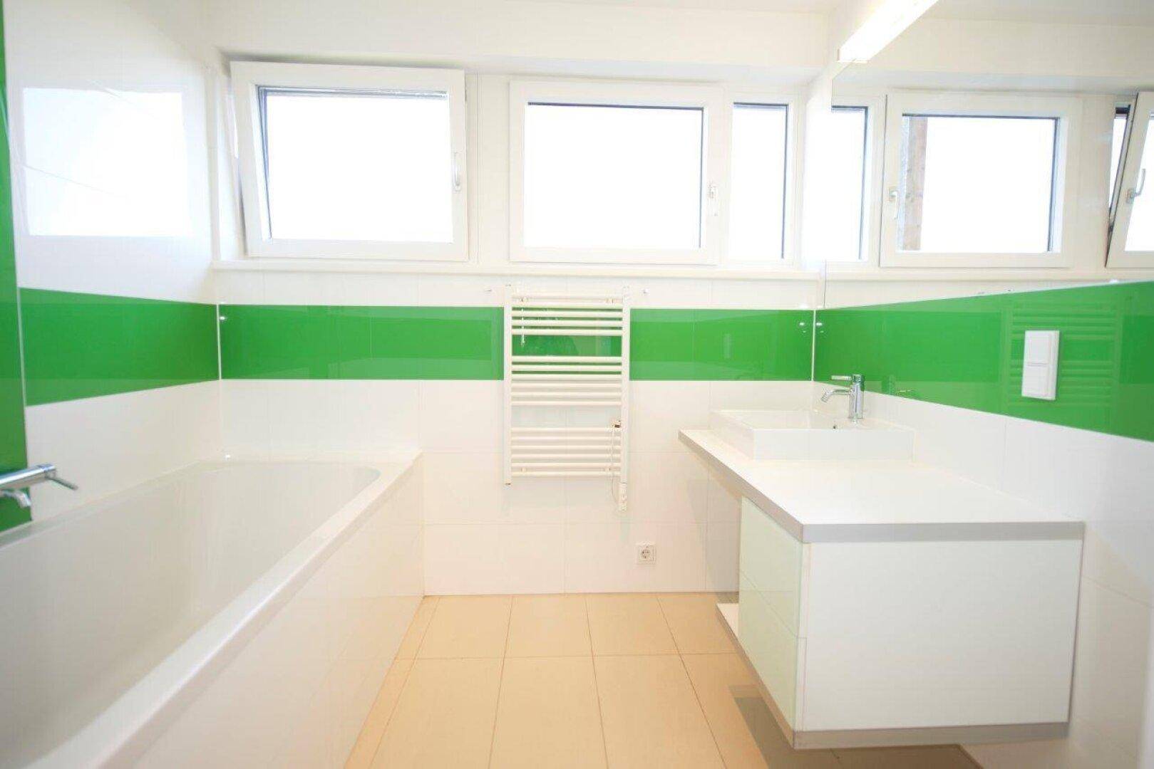 Modernes Badezimmer mit Badewanne, Doppelwaschbecken und grünen Akzenten.