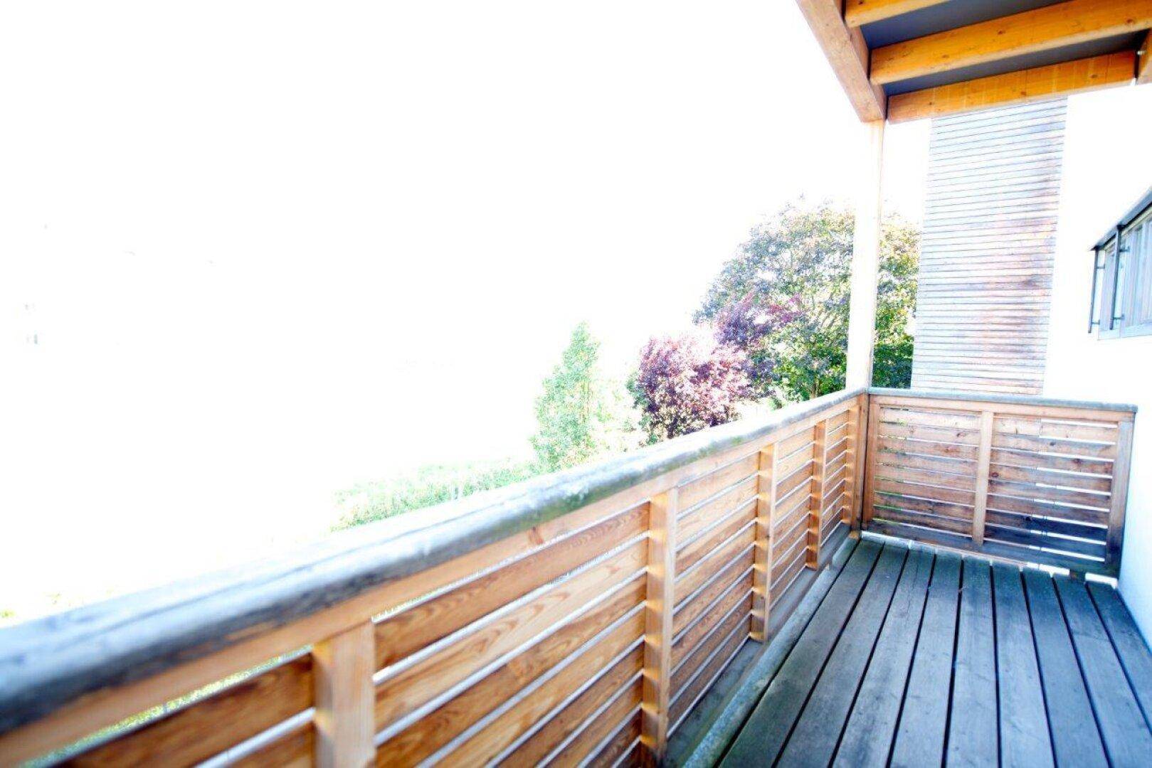 Heller Balkon mit Holzboden und Geländer, bietet einen weiten Blick ins Grüne.