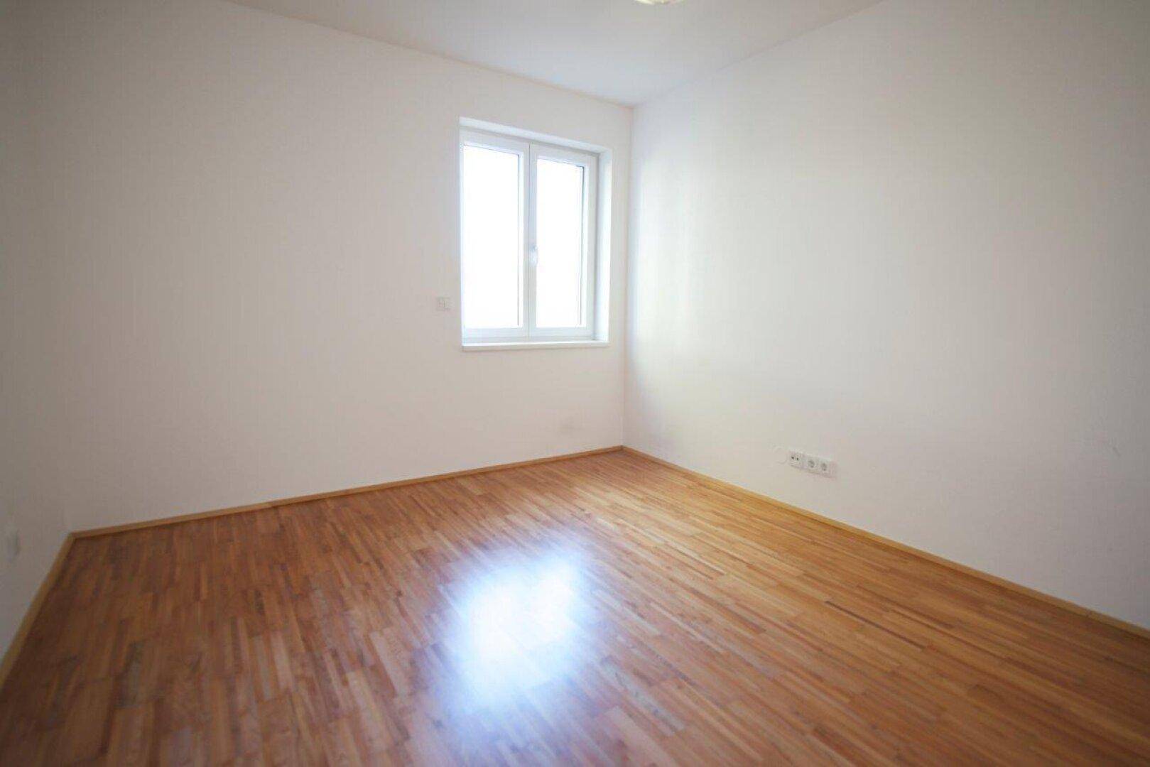 Schlafzimmer mit Parkettboden und großem Fenster, ideal für natürliche Belichtung.