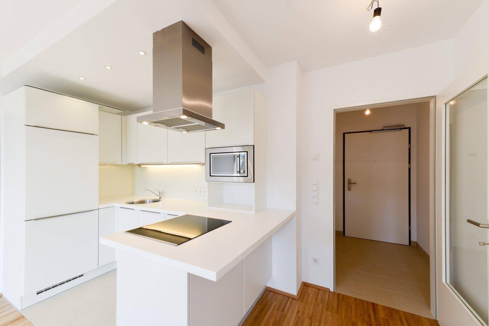 Moderne Einbauküche in Weiß mit Kochinsel und Edelstahlgeräten.