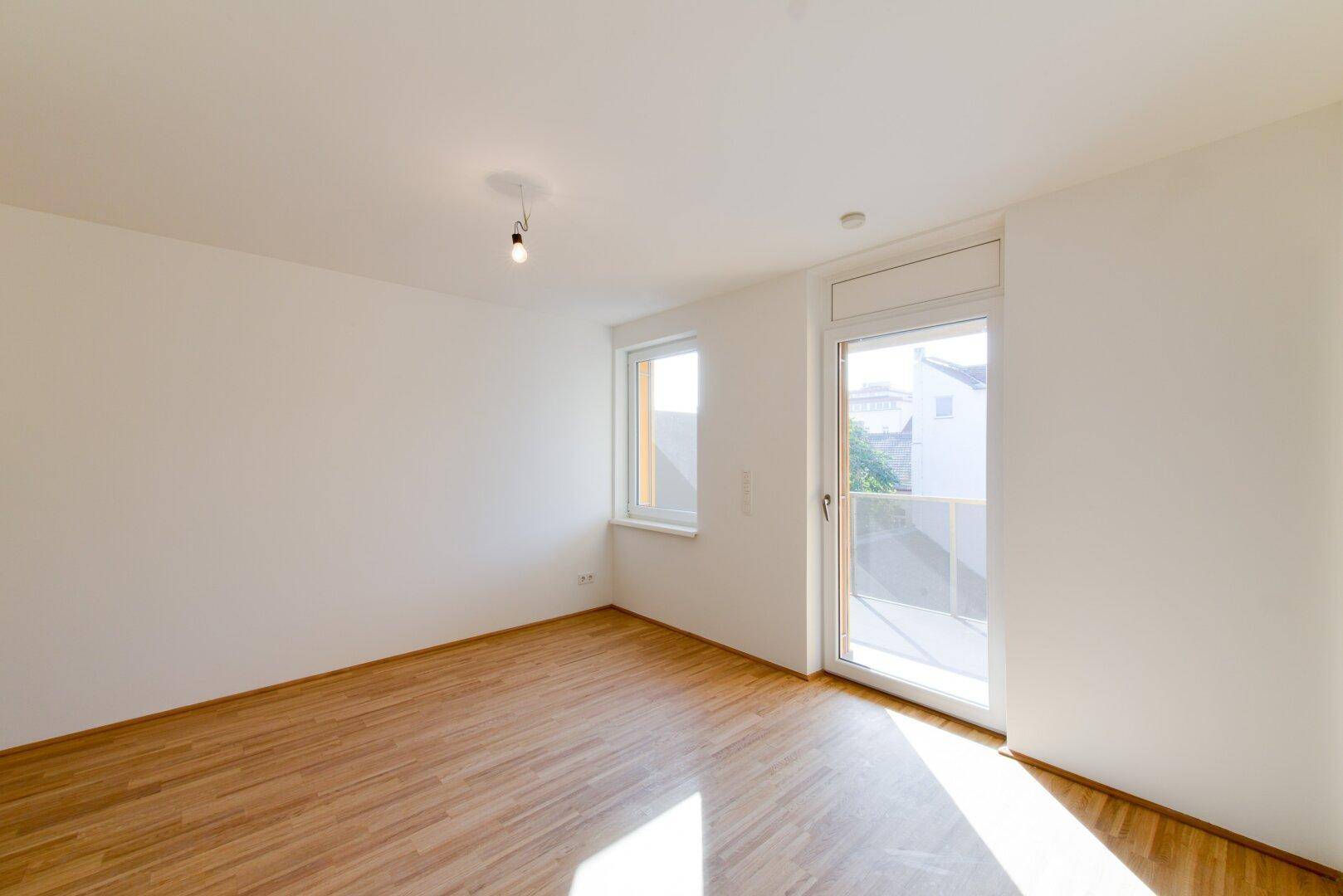 Heller Raum mit Parkettboden und Zugang zu einem Balkon, ideal als Wohn- oder Schlafzimmer.