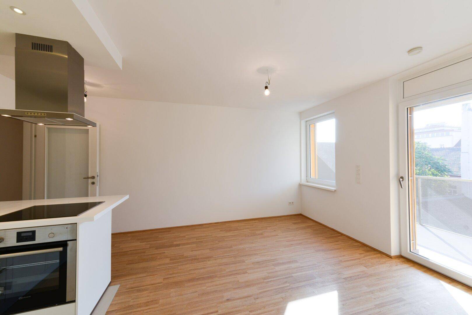 Offener Wohnbereich mit Küchenzeile und direktem Zugang zum sonnigen Balkon.
