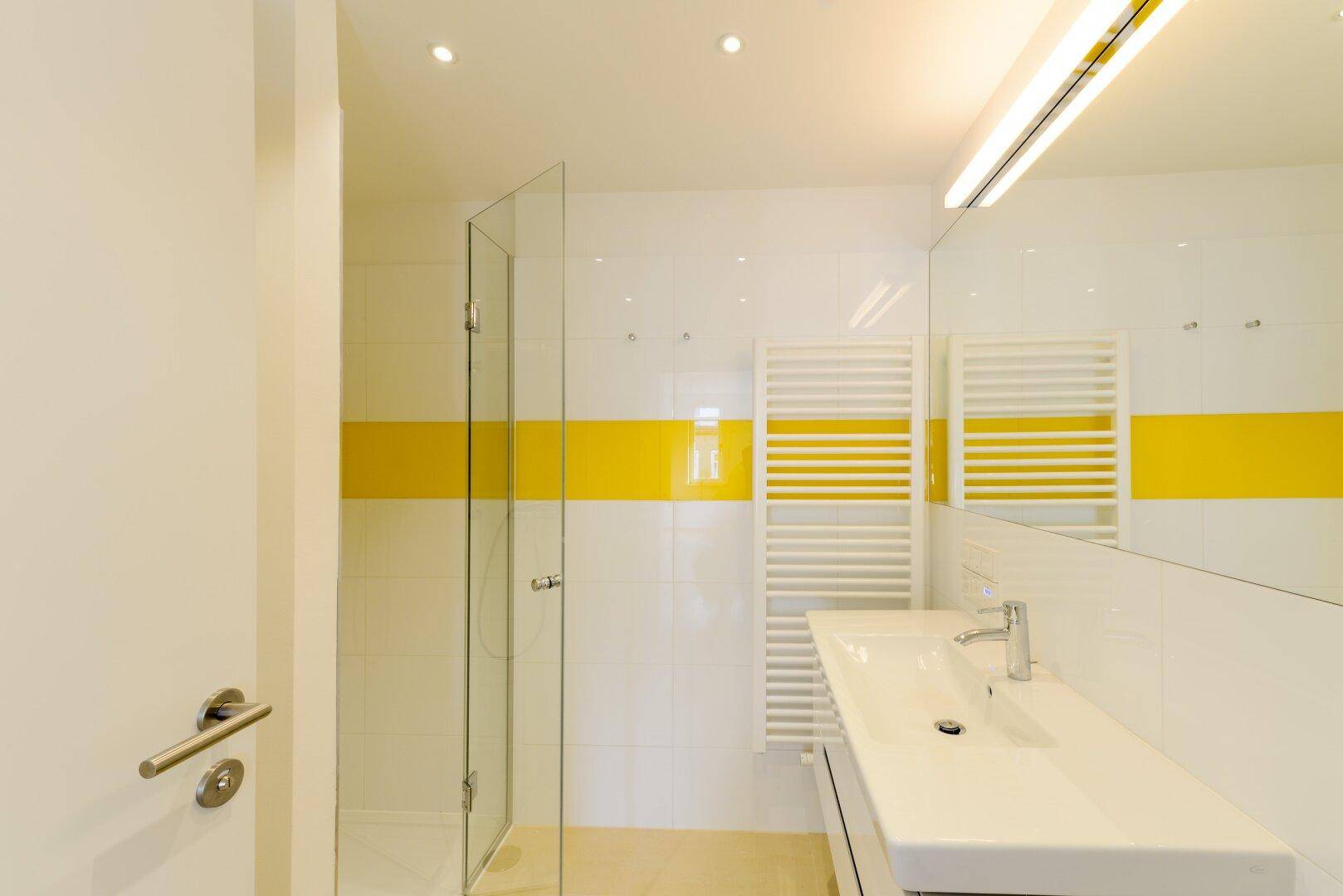 Modernes Badezimmer mit weiß-gelben Fliesen, Waschtisch und beheiztem Handtuchhalter.