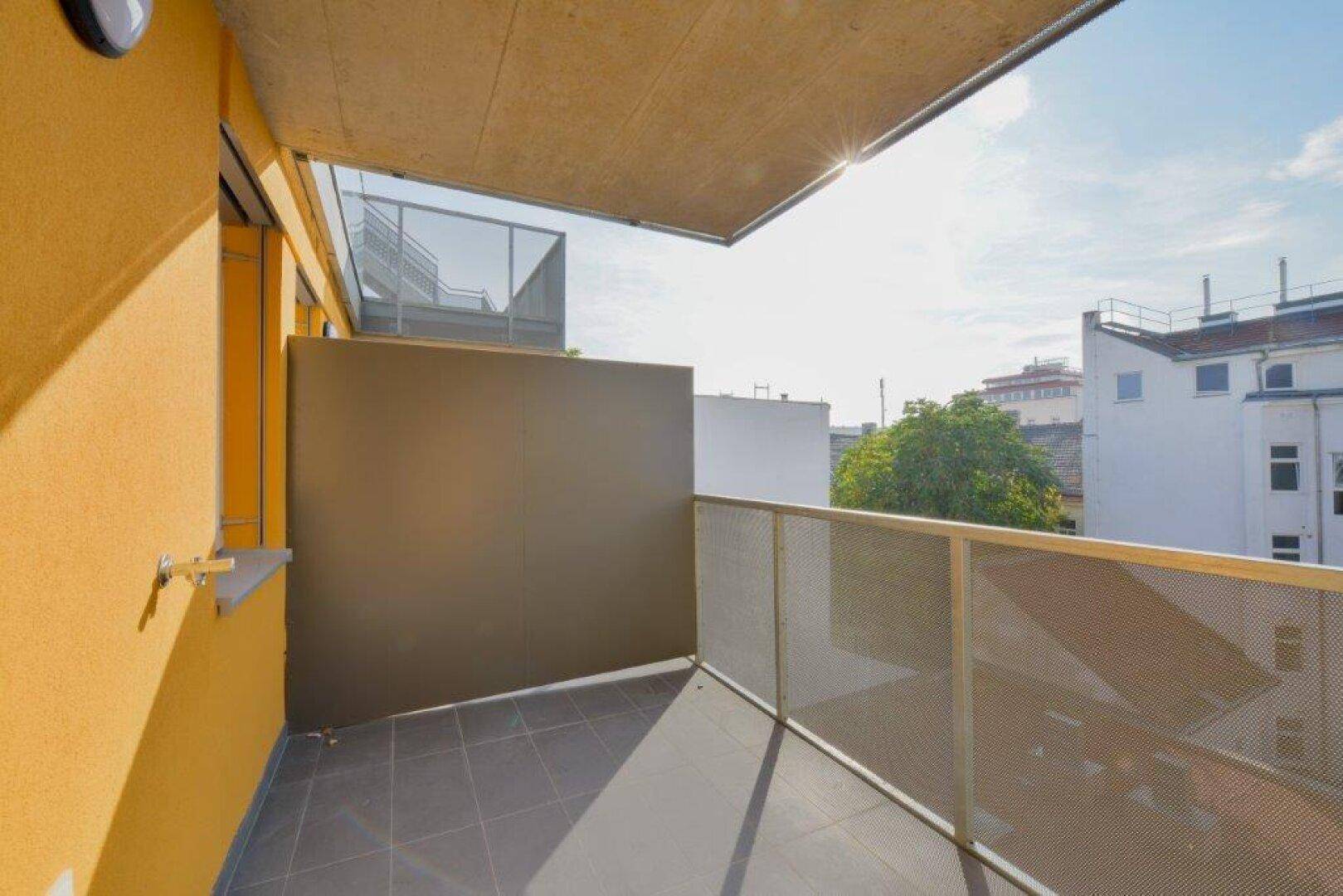 Sonnige Loggia mit Fliesenboden und Blick auf die umliegenden Gebäude.