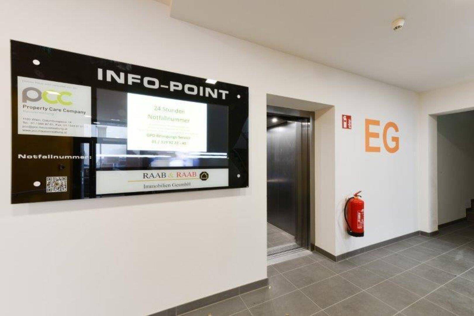 Moderner Eingangsbereich mit Aufzug, Informationsbildschirm und Brandschutzvorrichtungen.