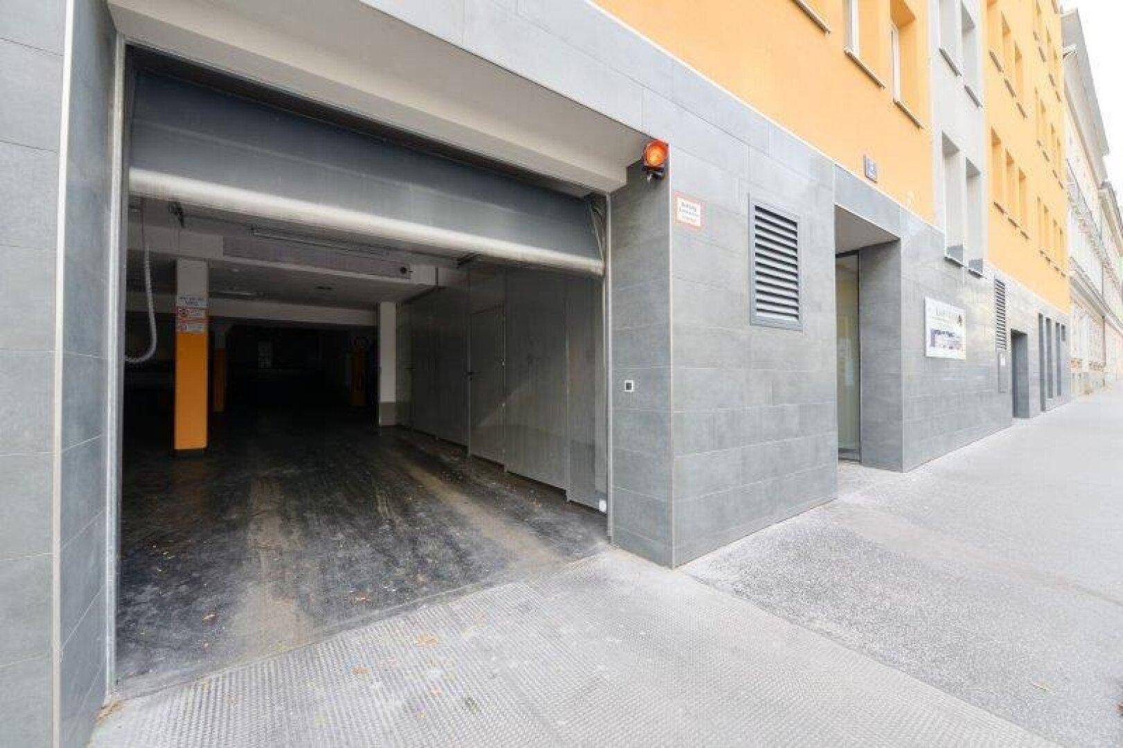 Einfahrt zur Tiefgarage des Gebäudes mit grauen Fliesen und gelber Fassade.