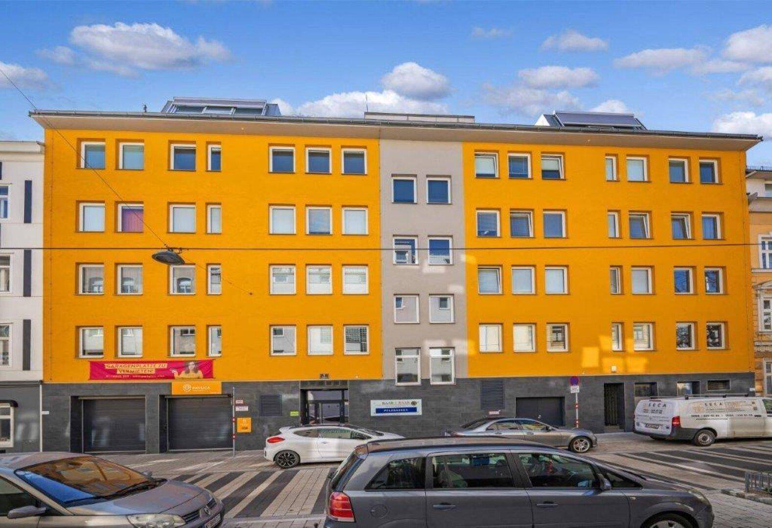 Ansicht der gelben Gebäudefassade mit vielen Fenstern und geparkten Autos davor.