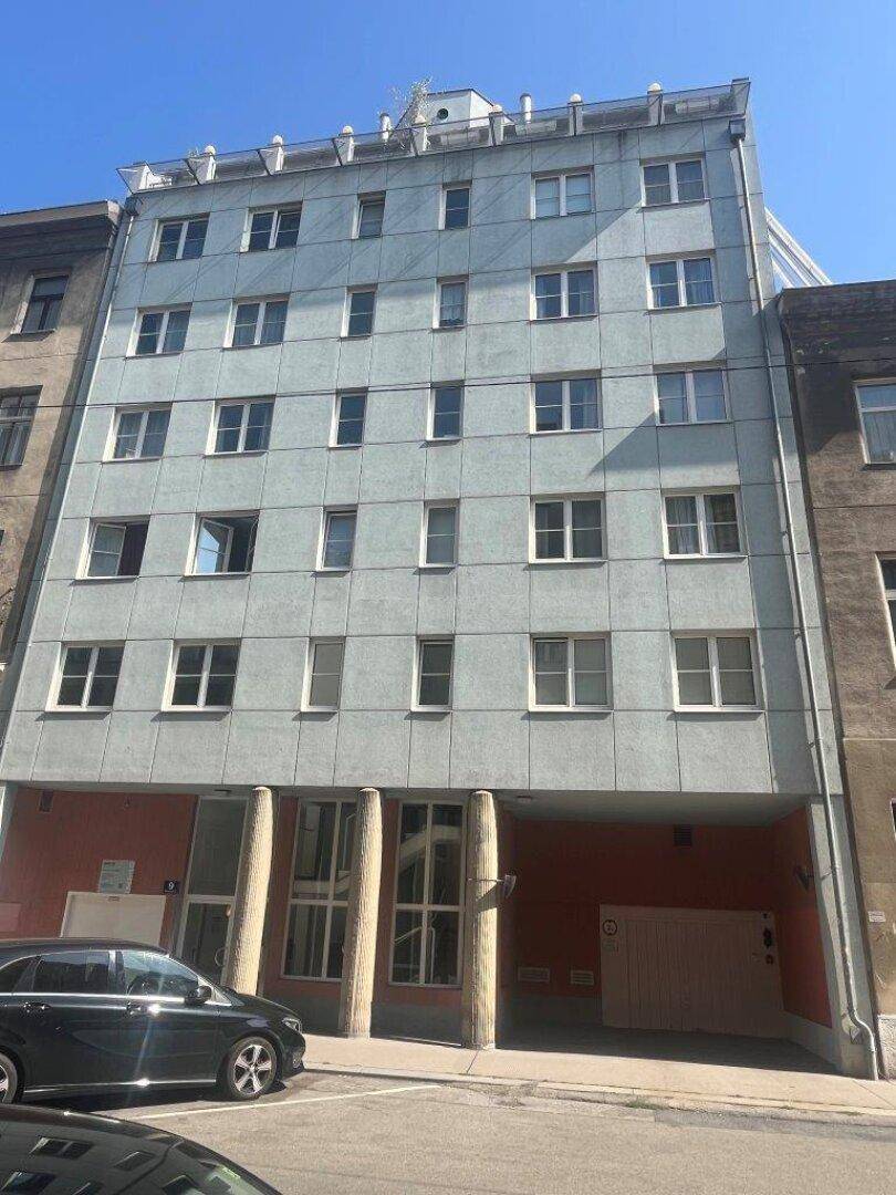 Ansicht der modernen Gebäudefassade mit hellblauen Paneelen und großen Fenstern in urbaner Umgebung.