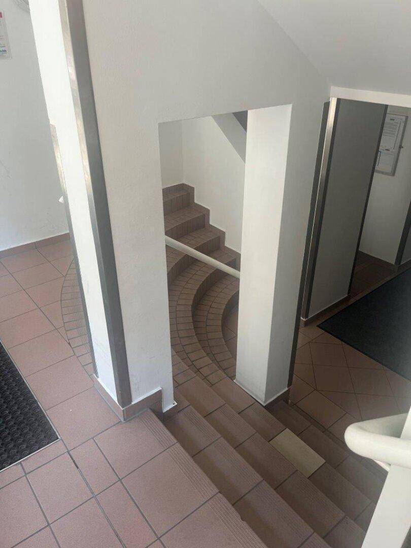 Treppenhaus mit Fliesenboden und weiß gestrichenen Wänden, das zu verschiedenen Wohneinheiten führt.