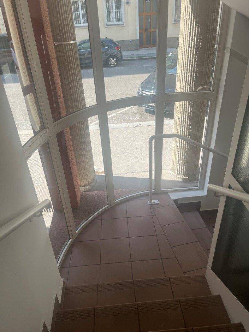 Heller Eingangsbereich mit Fliesenboden, Säulen und Treppe, die zu den oberen Etagen führt.