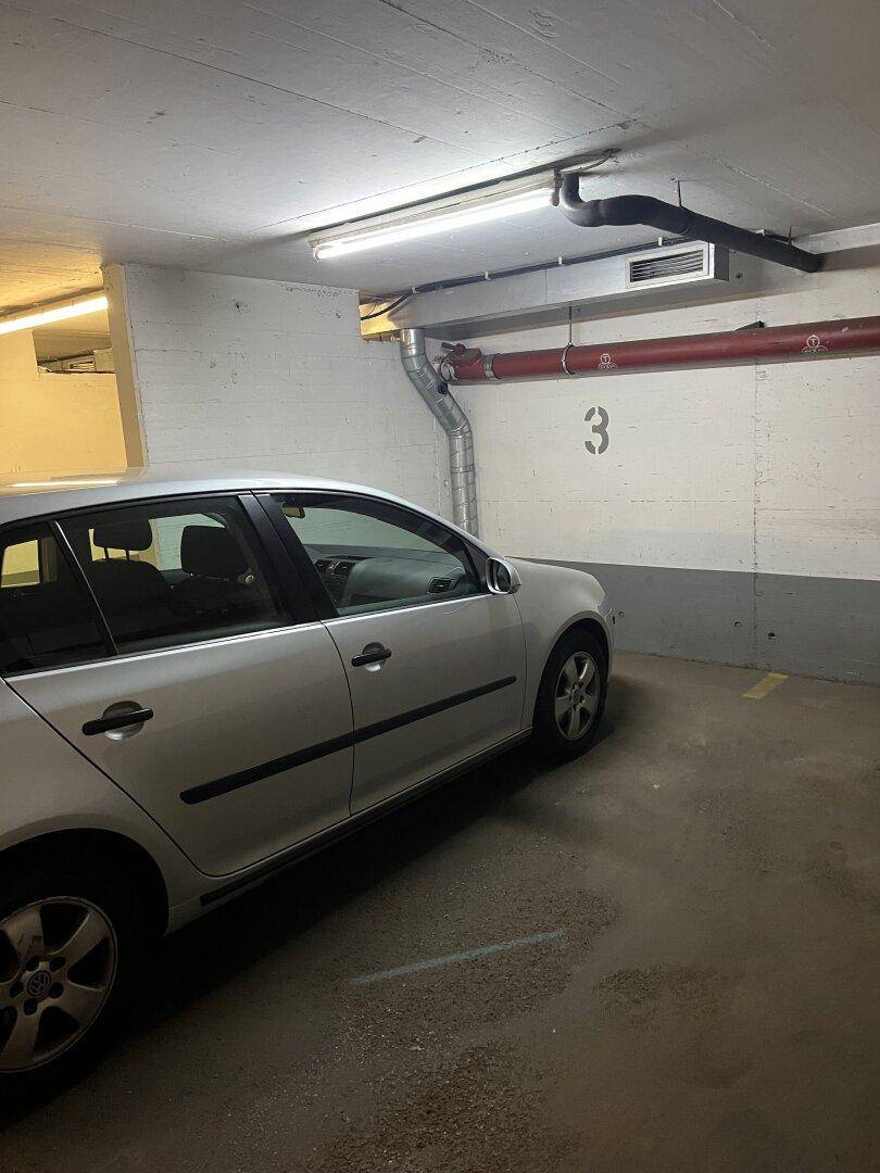 Tiefgarage mit einem geparkten Auto und sichtbaren Leitungen an der Decke.