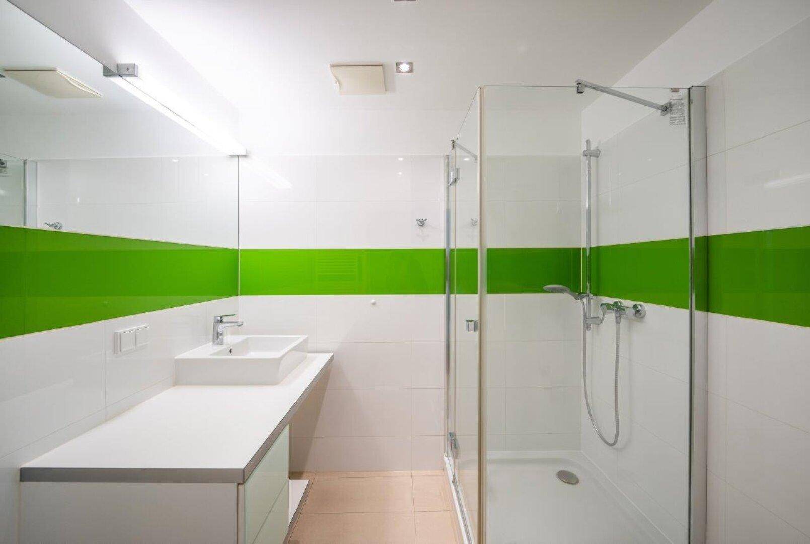 Modernes Badezimmer mit grüner Akzentwand, ebenerdiger Dusche und großem Spiegel.
