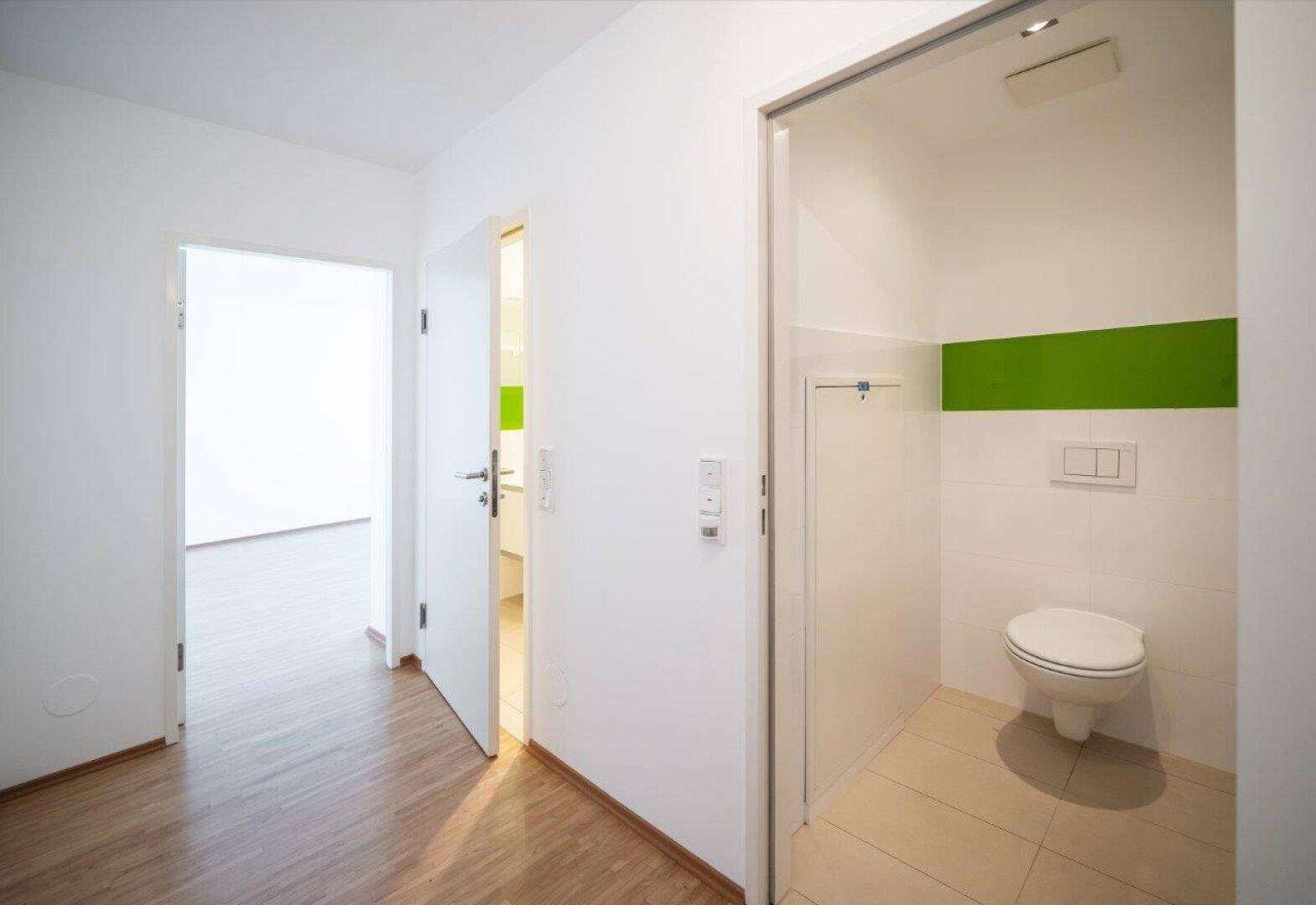 Heller Flur mit Zugang zu einem modernen Gäste-WC mit Wand-WC und grüner Akzentwand.