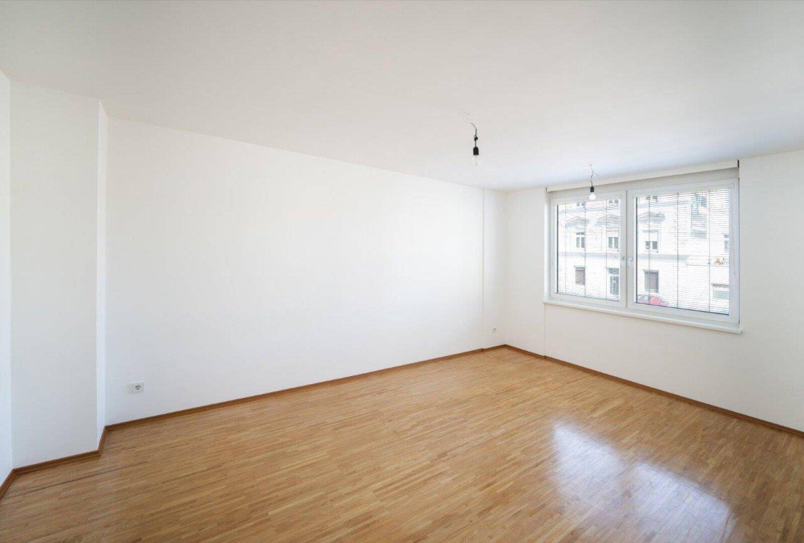 Geräumiges, leeres Zimmer mit Parkettboden und großen Fenstern für viel Tageslicht.