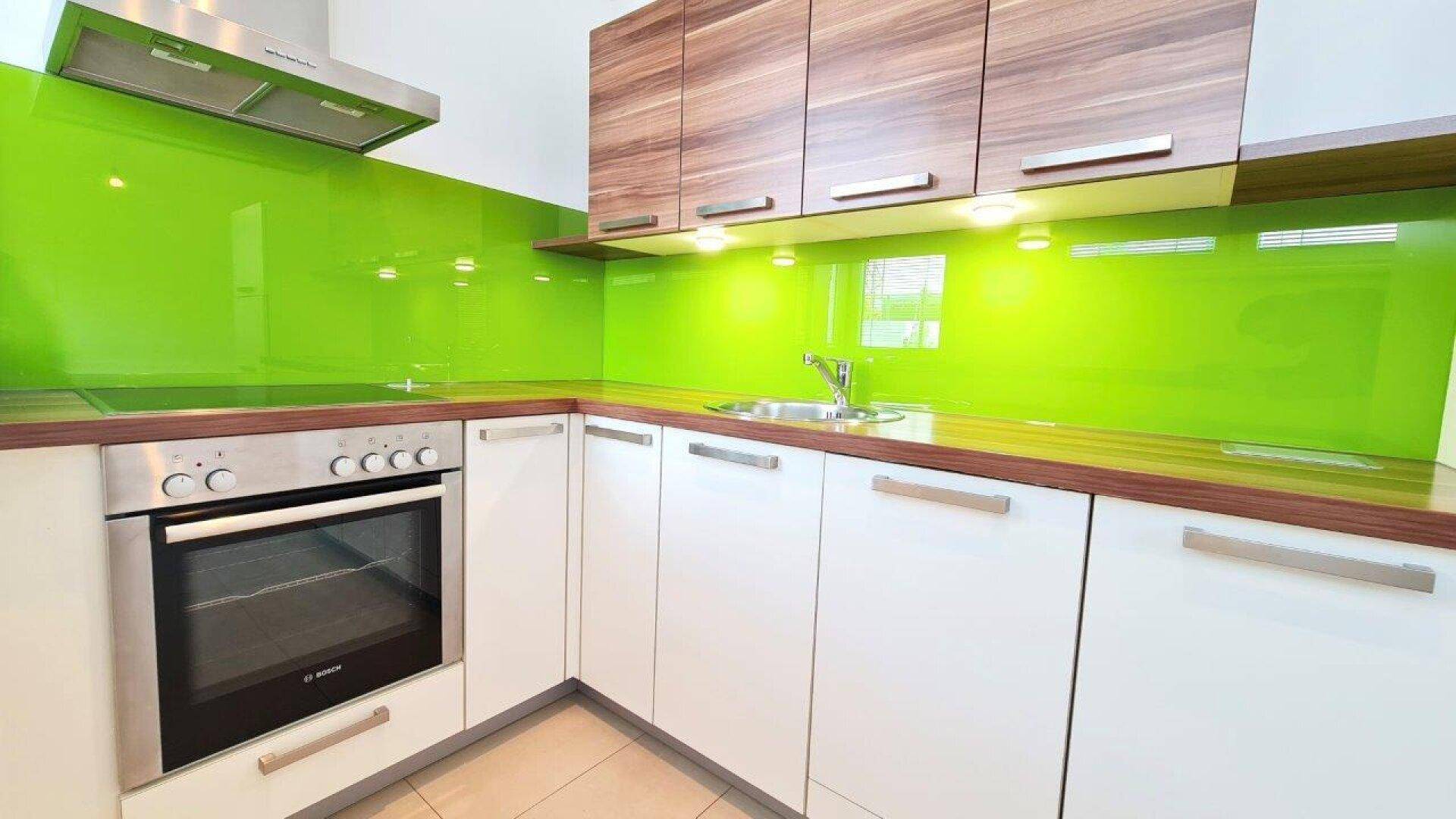 Helle Einbauküche mit grüner Glasrückwand, Holzoptik-Arbeitsplatte und modernen Geräten.