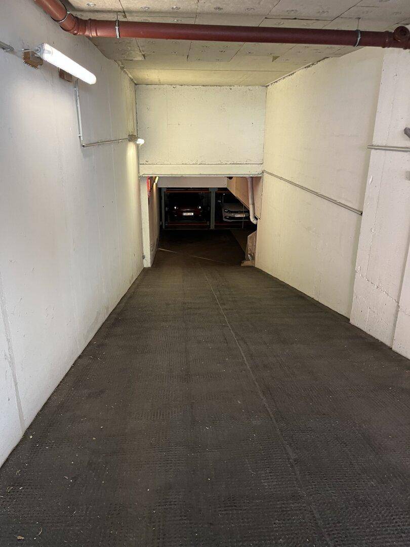 Dunkle Zufahrtsrampe zu einer Tiefgarage mit begrenzter Beleuchtung und Betonwänden.