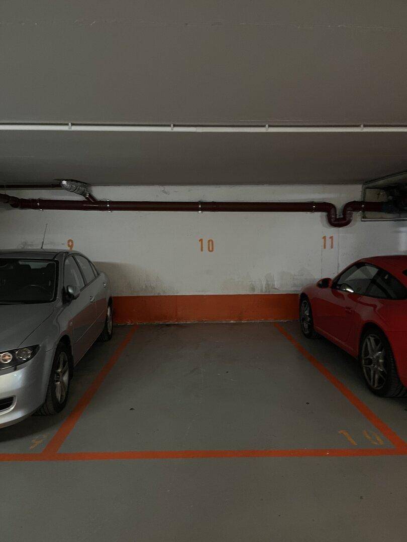 Zwei nummerierte Stellplätze in einer Tiefgarage mit geparkten Autos und Betonboden.