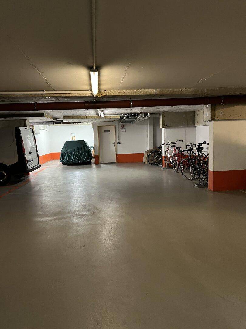 Bereich einer Tiefgarage mit einem Lieferwagen, einem abgedeckten Auto und mehreren Fahrrädern.