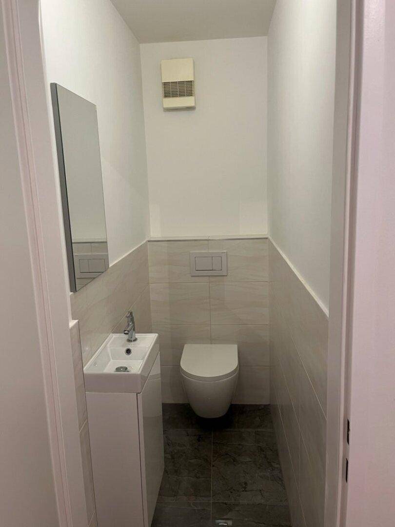 Modernes Gäste-WC mit wandhängender Toilette und kleinem Waschtisch, hell gefliest und platzsparend.