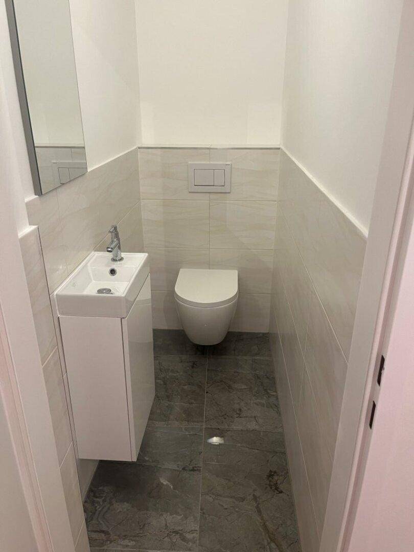 Gäste-WC mit modernem Design, wandhängender Toilette und kleinem Waschtisch, mit dunklem Boden.