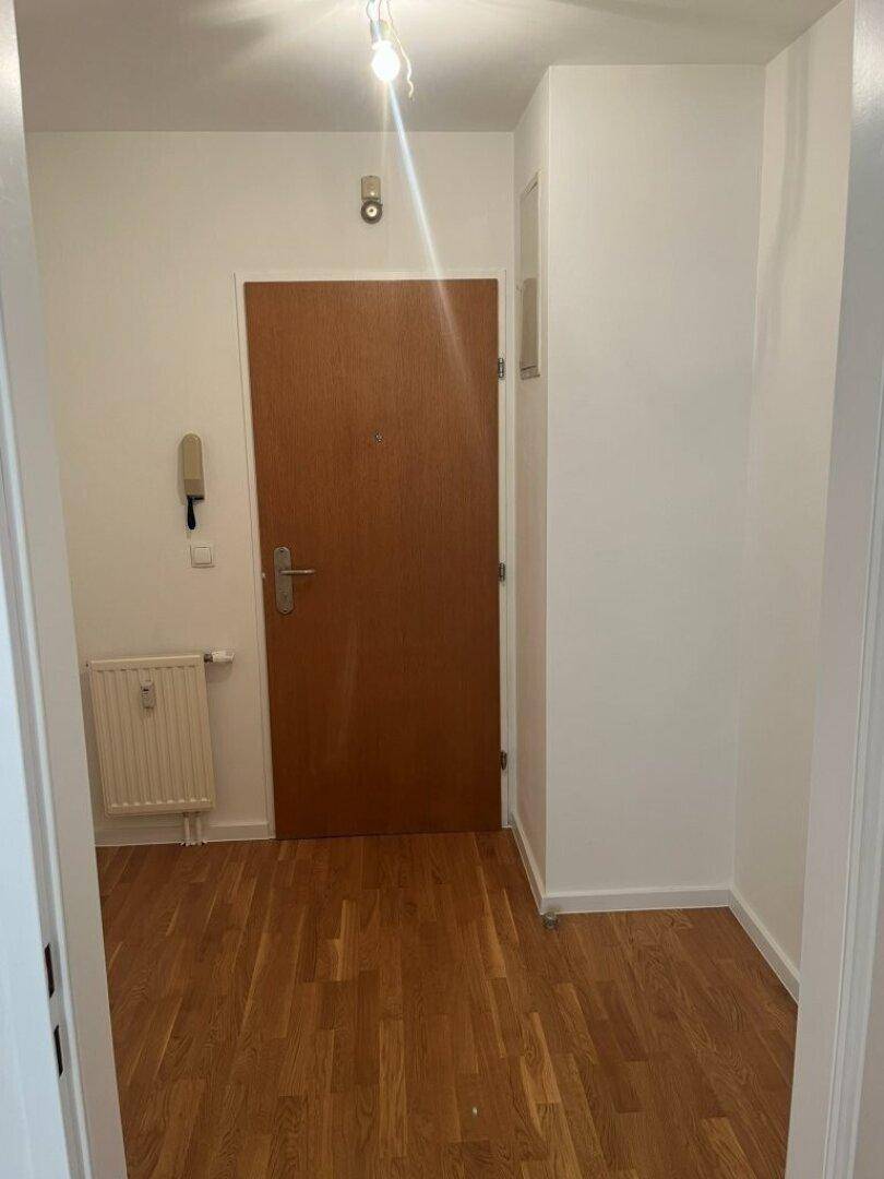 Eingangsbereich mit Holztür, Gegensprechanlage und hellem Parkettboden, der in andere Räume führt.